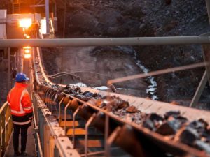 Shallow depth of field image of a miner inspecting ore rocks on a conveyor